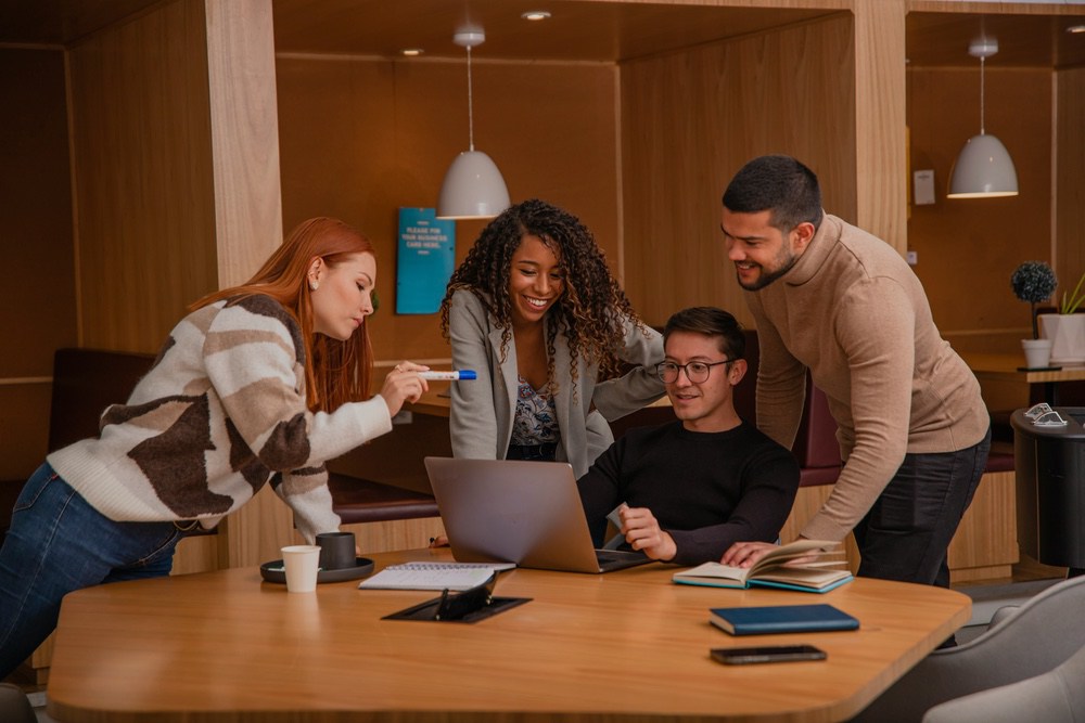Four colleagues gathered around a laptop in a cafe-style workspace