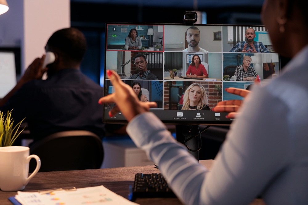 Two coworkers on a video call with a grid of remote attendees on screen